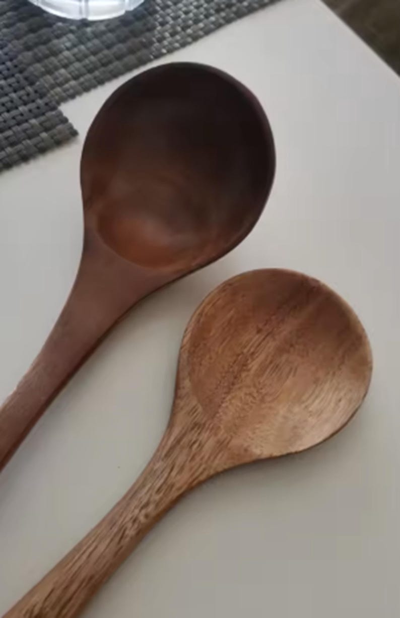 May include: Two wooden spoons with long handles and rounded bowls. One spoon is a dark brown color, while the other is a lighter, natural wood tone. The spoons are likely for cooking or serving.