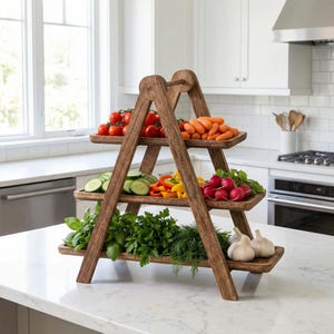 Puede incluir: Una bandeja de madera de tres niveles, con forma de escalera, llena de productos frescos. El nivel superior contiene tomates rojos y zanahorias naranjas. El nivel intermedio tiene pepinos en rodajas, pimientos rojos y amarillos y rábanos rojos. El nivel inferior muestra hierbas frescas y ajo.