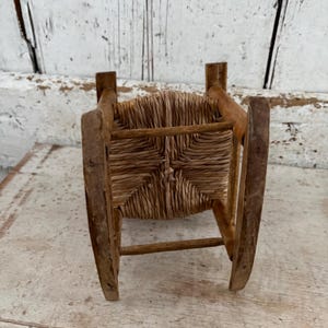 May include: A miniature wooden rocking chair with a woven straw seat. The chair is made of light brown wood and has a classic design. The seat is square and woven with a natural fibre. The chair is a miniature size.