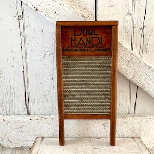 Op de afbeelding: Een vintage houten wasbord met een bruin frame en een gegolfd metalen schrobvlak. Het bovenste gedeelte heeft de tekst "DUBL HANDI" in een donker lettertype. Het wasbord is een klassiek wasgereedschap.
