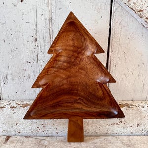 May include: A wooden Christmas tree-shaped serving dish. The dish is made of dark brown wood with a natural grain pattern. It has a deep bowl and a sturdy base.