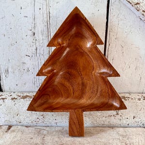 May include: A wooden Christmas tree-shaped serving dish. The dish is made of dark brown wood and has a natural, rustic finish.