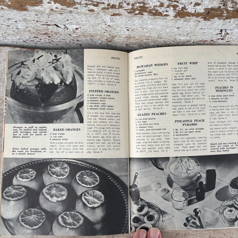 May include: A vintage cookbook page featuring recipes for fruit-based desserts. The page includes instructions for baked oranges, stuffed oranges, Hawaiian wedges, fruit whip, glazed peaches, pineapple peach pyramid, and peaches in meringues. The image is in black and white.