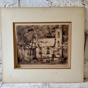 May include: A black and white etching on paper featuring a church building with a tall tower and a graveyard in the foreground. The artwork is titled Old Levens Church and signed by the artist, matted in a light beige frame with a rectangular border.