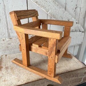 Peut inclure: Petite chaise &agrave; bascule en bois faite &agrave; la main, avec une finition naturelle. La chaise comprend une assise &agrave; lattes, des accoudoirs et un dossier. Fabriqu&eacute;e en bois brun clair, elle est con&ccedil;ue &agrave; des fins d&eacute;coratives.