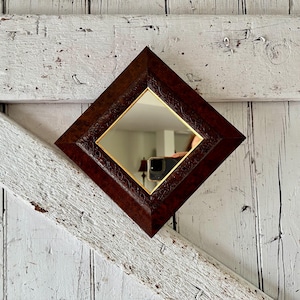 以下が含まれることがあります： 濃い茶色のフレームと金色の縁取りが施されたダイヤモンド型の鏡。フレームには複雑なデザインが施されています。