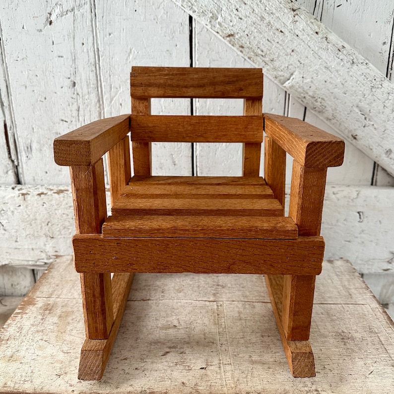 Peut inclure: Petite chaise &agrave; bascule en bois avec une finition naturelle. Le si&egrave;ge et le dossier sont &agrave; lattes, avec des accoudoirs. La chaise est en bois et est con&ccedil;ue &agrave; des fins d&eacute;coratives. Une version miniature d'une chaise &agrave; bascule classique.