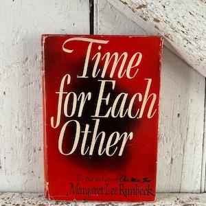 May include: A vintage book titled "Time for Each Other" with a red cover and white lettering. The author's name, Margaret Lee Runbeck, is printed at the bottom. The book is set against a distressed white wooden background.