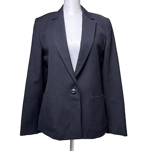 May include: A solid black blazer featuring a single-button front closure, notched lapels, and two large patch pockets on the lower front. The garment has long sleeves and a structured fit, displayed on a white mannequin torso against a white background.