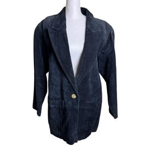 May include: A dark charcoal gray suede blazer featuring a notched lapel collar, long sleeves, and a single gold-toned metal button closure at the front. The jacket includes two front flap pockets and a structured silhouette with visible seam detailing.