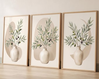 May include: A set of three framed wall art prints, each featuring a white ceramic vase containing olive branches with green and black olives. The background of each print displays a soft beige abstract shape, and the frames are light wood.