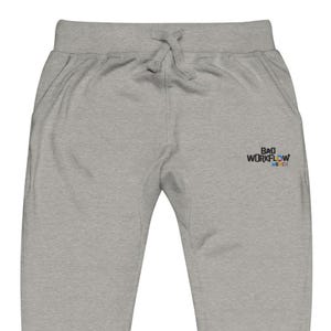 May include: Light grey sweatpants with a drawstring waist and pockets. The text "BAD WORKFLOW MERCH" is embroidered in a small, colourful design on the upper left leg. These pants are a casual apparel item.