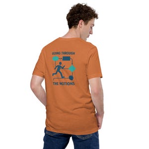 May include: Orange t-shirt featuring the text "GOING THROUGH THE MOTIONS" and a diagram of a stick figure running through shapes. The shirt is a solid orange colour and is being worn by a person.