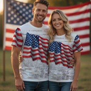 Puede incluir: Dos personas vestidas con camisetas blancas con un diseño patriótico. Las camisetas presentan una gran bandera estadounidense y texto de la Declaración de Independencia. Las mangas tienen rayas rojas y blancas. Están de pie frente a una bandera estadounidense.