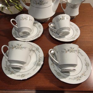 May include: A white porcelain tea set with floral detailing. The set includes a teapot, creamer, sugar bowl, and four teacups with saucers. Each piece has a silver trim and delicate floral pattern, creating an elegant aesthetic.
