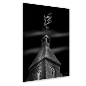 Puede incluir: Fotografía en blanco y negro de una torre de iglesia de piedra con una veleta. La veleta presenta figuras y puntos cardinales. La torre tiene ventanas arqueadas y un tejado de piedra, sobre un cielo oscuro.