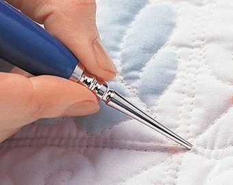 May include: A close-up of a hand using a blue and silver quilting tool to smooth out a white quilted fabric.