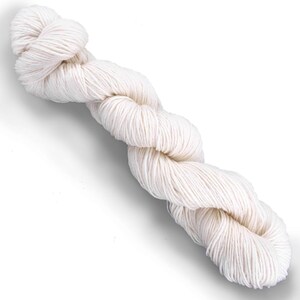 Puede incluir: Una madeja de hilo color blanco hueso retorcida en una bobina larga y continua. El hilo presenta una textura suave de m&uacute;ltiples cabos con un color crema claro consistente en toda la longitud de la fibra, sobre un fondo blanco liso.