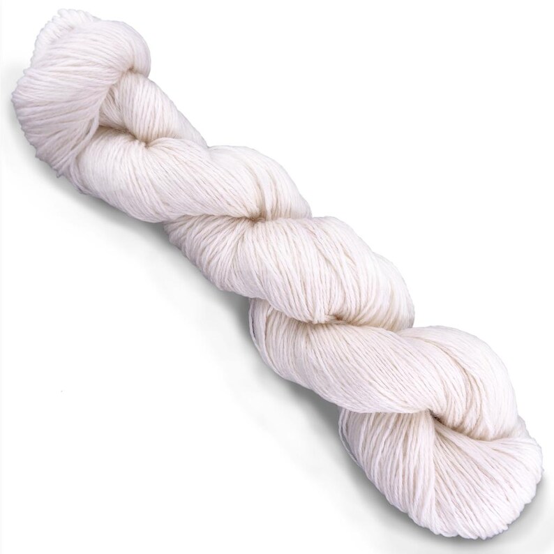 Puede incluir: Una madeja de hilo retorcido de color blanco roto. La fibra est&aacute; enrollada en un bucle largo y continuo con una textura suave y mate, presentando un color crema claro uniforme en toda la longitud del hilo retorcido.