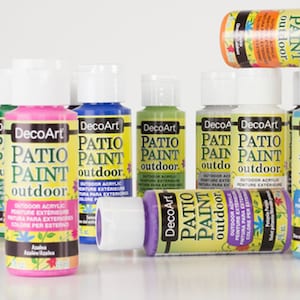 May include: Assortment of eight bottles of DecoArt Patio Paint in various colors, including pink, blue, green, white, and purple. Each bottle has a yellow label with the text "DecoArt Patio Paint outdoor" and details about the paint.