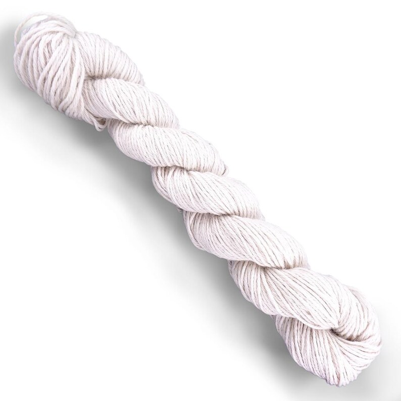 Puede incluir: Una madeja de hilo color blanco roto retorcida en una forma cil&iacute;ndrica alargada. El hilo presenta una construcci&oacute;n de m&uacute;ltiples cabos con una torsi&oacute;n texturizada visible a lo largo de toda la fibra, presentado sobre un fondo blanco liso.
