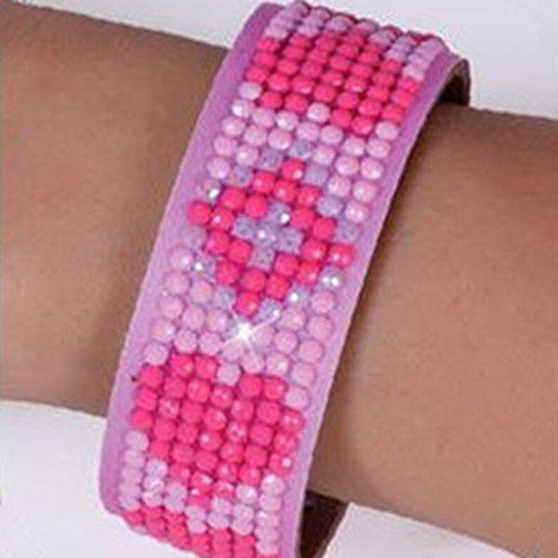 May include: A pink and fuchsia beaded bracelet with a diamond-like pattern. The bracelet is made of small, round beads that are arranged in a geometric design.