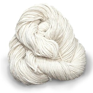 Puede incluir: Una madeja de hilo color blanco roto enrollada en un paquete redondo y suelto. El hilo presenta una construcci&oacute;n trenzada de varias hebras con una textura mate, mostrando un color crema claro uniforme en toda la longitud de la fibra.