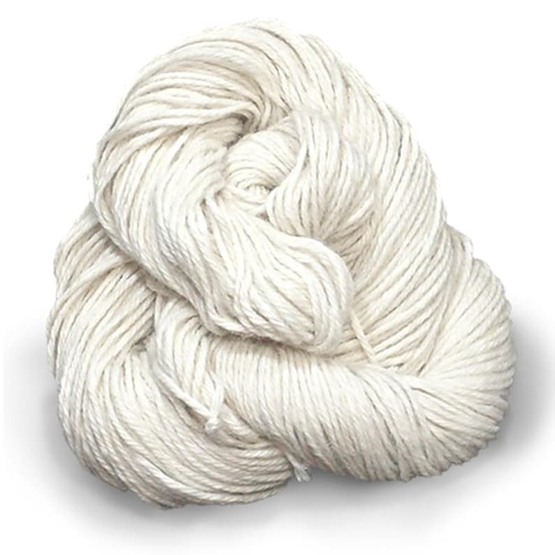 Puede incluir: Una madeja de hilo color blanco roto enrollada en un paquete redondo y suelto. El hilo presenta una construcci&oacute;n trenzada de varias hebras con una textura mate, mostrando un color crema claro uniforme en toda la longitud de la fibra.
