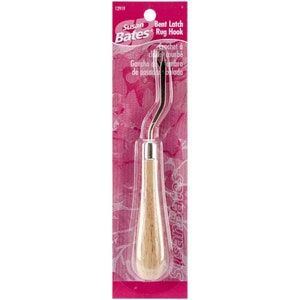 May include: A bent latch rug hook with a wooden handle. The hook is silver and has a curved shape. The packaging is pink and features the Susan Bates brand name.