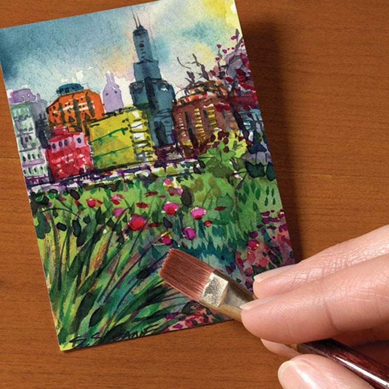 May include: A watercolor painting of a cityscape with tall buildings and a green park in the foreground. The painting is being worked on with a paintbrush.
