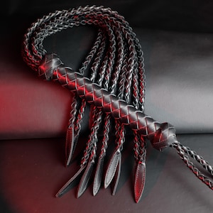 Puede incluir: Un látigo de cuero negro con un mango trenzado y múltiples hebras trenzadas. El látigo está hecho de cuero oscuro y tiene una apariencia texturizada. El mango también está trenzado y los extremos de las hebras tienen una forma lisa y redondeada.