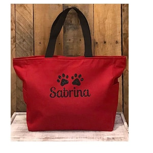 May include: Red canvas tote bag with black handles and a black paw print design. The bag is personalized with the name "Sabrina".