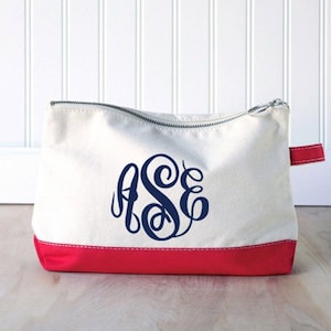 May include: A white canvas zippered pouch with a red bottom. The pouch has a navy blue monogram of the letters "ASE" on the front.