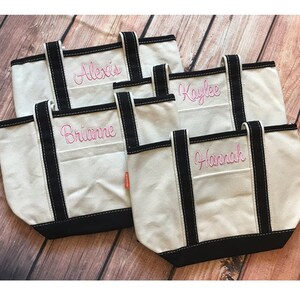 May include: Four white canvas tote bags with black trim and pink embroidered names: Alexis, Kaylee, Brianne, and Hannah.