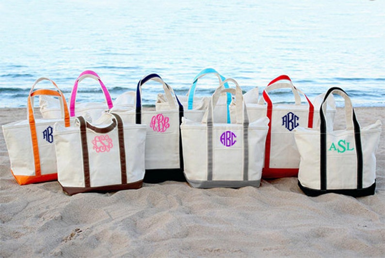 May include: Eight canvas tote bags with different colored handles and trim. Each bag has a monogram embroidered on the front.