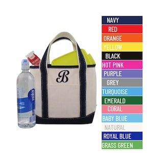 May include: A white canvas tote bag with navy blue trim and a navy blue embroidered letter "B". The bag is filled with a water bottle and a peanut butter packet. The image also shows a color chart with various colors, including navy, red, orange, yellow, black, hot pink, purple, grey, turquoise, emerald, coral, baby blue, natural, royal blue, and grass green.