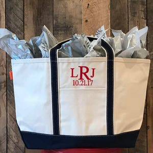 May include: A white canvas tote bag with navy blue trim and handles. The bag has a red embroidered monogram "LRJ" and the date "10.21.17".