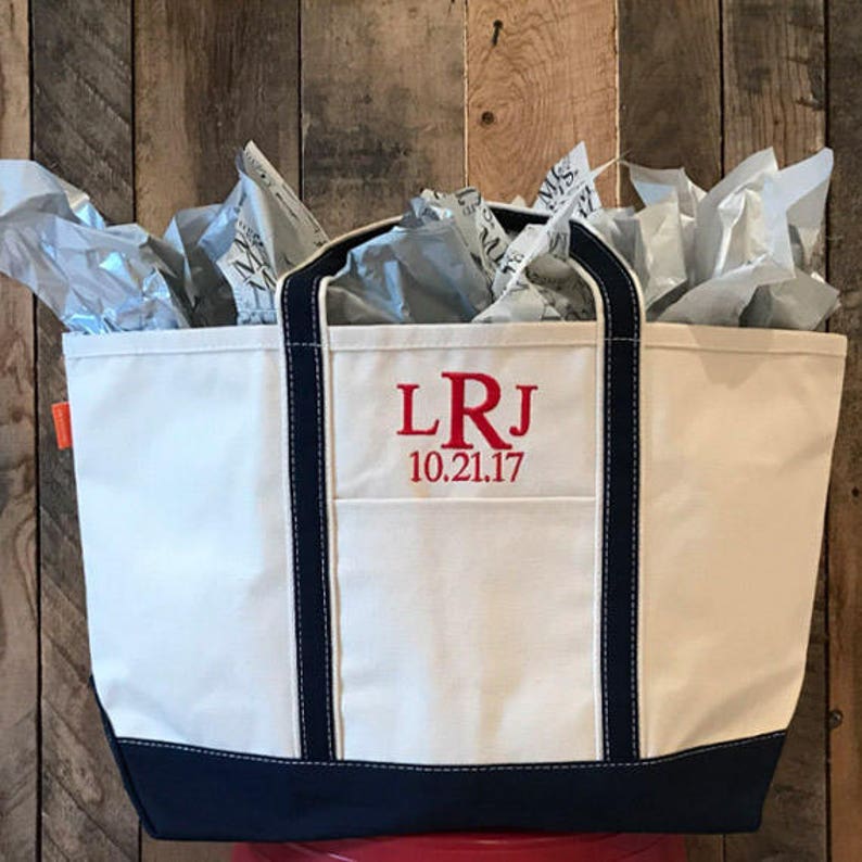 May include: A white canvas tote bag with navy blue trim and handles. The bag has a red embroidered monogram "LRJ" and the date "10.21.17".