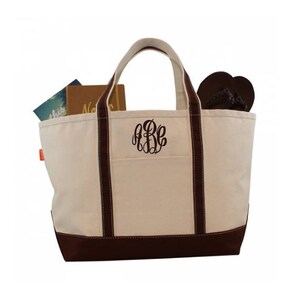 May include: A large, cream-colored canvas tote bag with brown trim and handles. The bag has a large pocket on the front with a monogram in brown.