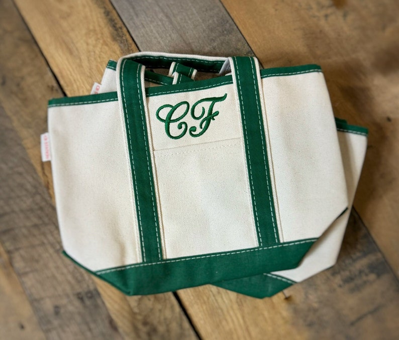 以下が含まれることがあります： 緑色の縁取りと、正面に緑色の刺繍で「CF」のイニシャルが入った白いキャンバス地のトートバッグです。