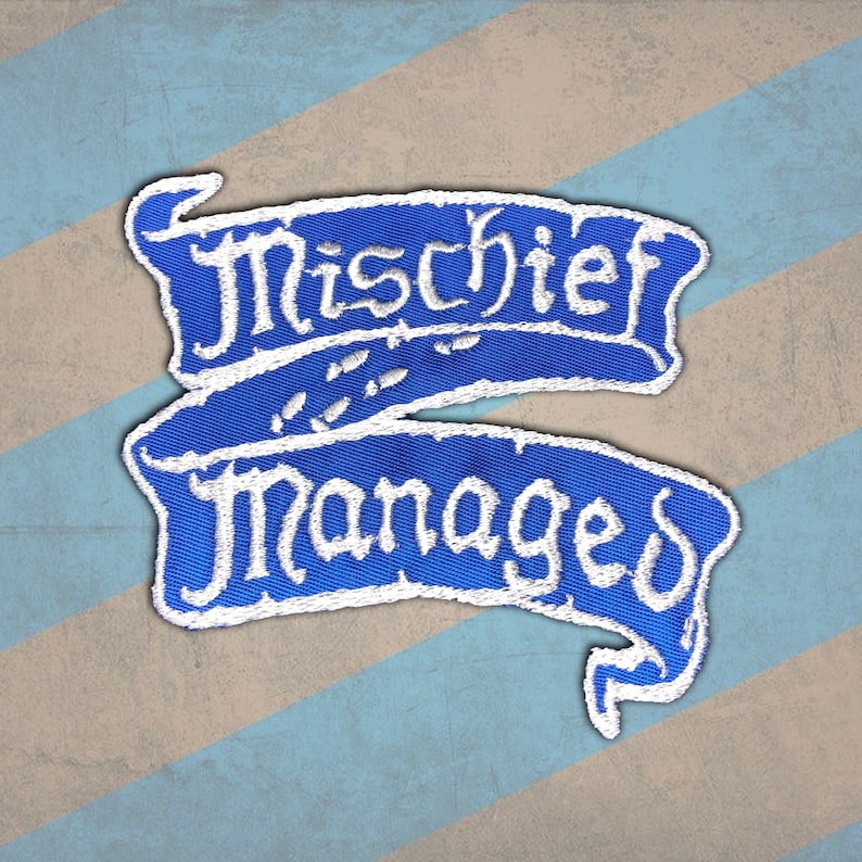 Peut inclure: Un &eacute;cusson brod&eacute; bleu avec les mots "Mischief Managed" en &eacute;criture blanche. L'&eacute;cusson a la forme de deux banni&egrave;res superpos&eacute;es. Le fond est un motif &agrave; rayures diagonales bleues et beiges.