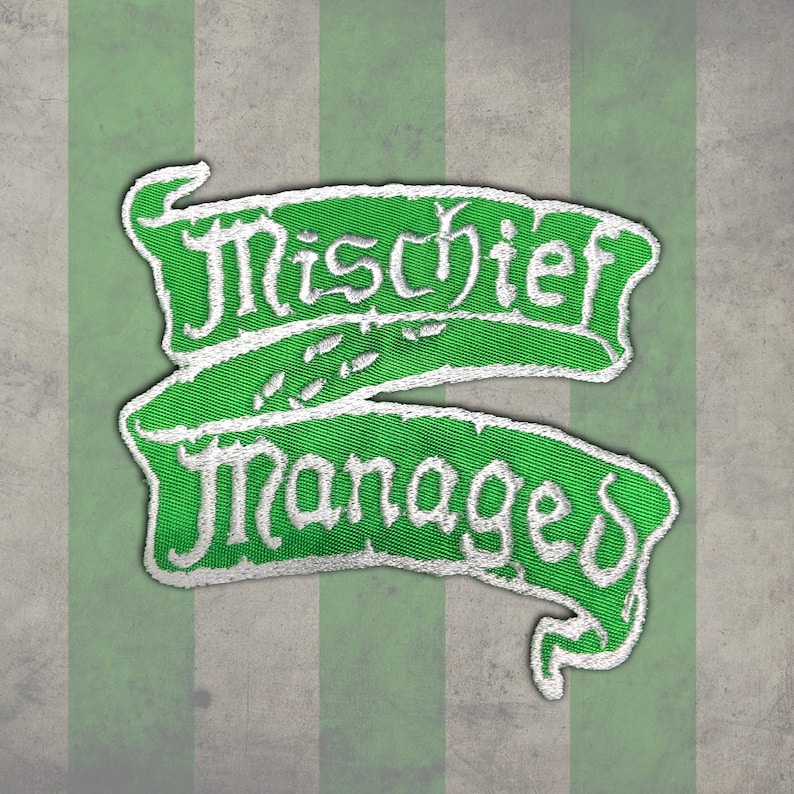 Peut inclure: &Eacute;cusson brod&eacute; vert avec les mots "Mischief Managed" en &eacute;criture blanche. L'&eacute;cusson a la forme d'une banni&egrave;re avec une bordure blanche. Le fond est un motif ray&eacute; vert et gris.