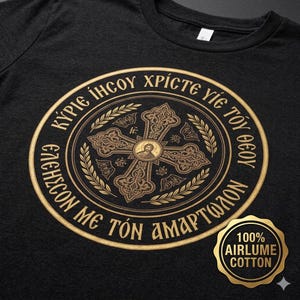 Könnte beinhalten: Dunkelgraues T-Shirt mit einem goldfarbenen, verzierten Kreuzdesign in einem kreisförmigen Rahmen. Das Design enthält griechischen Text und ein kleines Bild einer Person. Ein goldfarbenes Siegel unten rechts lautet "100% Airlume Cotton."
