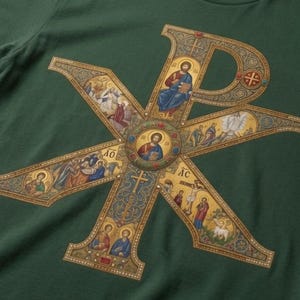 May include: A dark green t-shirt featuring a large, ornate Chi Rho symbol printed in gold, blue, and red. The design incorporates intricate religious iconography, including multiple small scenes of figures and crosses within the letter structure.