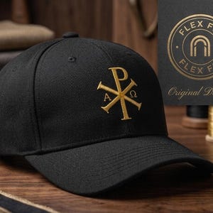 May include: A black baseball cap featuring an embroidered gold Chi Rho symbol on the front. The symbol includes the Greek letters Alpha and Omega. A black tag attached to the side displays the text FLEX FIT in a circular gold logo with the words Original Design.