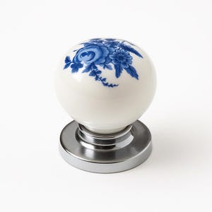 May include: A white ceramic door knob with a blue floral design. The knob is spherical and sits on a shiny, silver-coloured base. The floral pattern includes roses and other flowers.