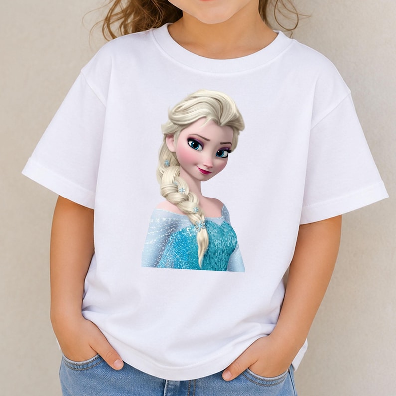 May include: A white short-sleeved t-shirt featuring a graphic print of a blonde character with a long braided hairstyle, wearing a blue dress with snowflake accents. The character has large blue eyes and is positioned in the center of the shirt.