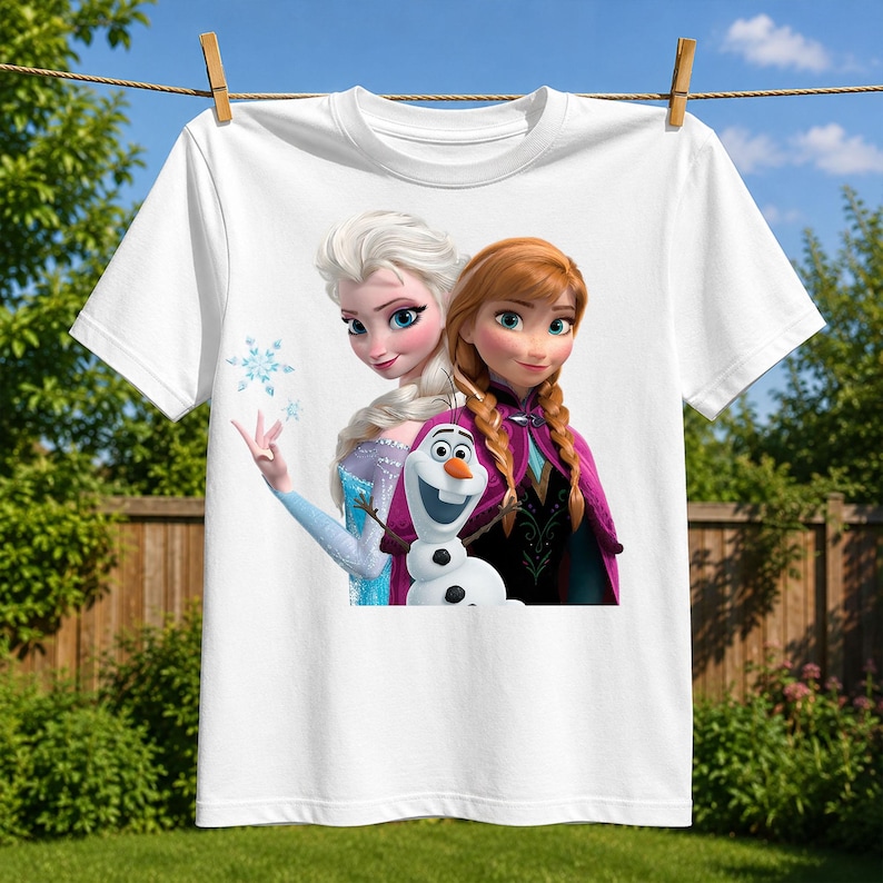 May include: A white short-sleeved t-shirt featuring a graphic print of the characters Elsa, Anna, and Olaf from the movie Frozen. Elsa is on the left with blonde hair, Anna is on the right with braided auburn hair, and Olaf is centered below.