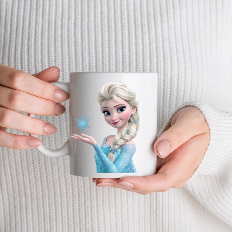 May include: A white ceramic mug featuring a printed graphic of a blonde character with a long braided hairstyle, wearing a light blue dress, and holding a small blue snowflake icon in an outstretched hand against a plain white background.