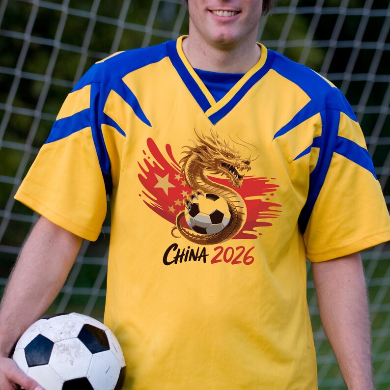 K&ouml;nnte beinhalten: Gelbes und blaues Fu&szlig;balltrikot mit einem Drachen- und Fu&szlig;ball-Design. Auf dem Trikot steht "CHINA 2026". Eine Person h&auml;lt das Trikot und einen Fu&szlig;ball.